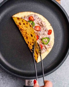 A single taco in a skillet being toasted and flipped with tongs.