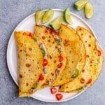 A close-up of four folded chicken tacos garnished with cherry tomatoes, jalapeños, and lime wedges.