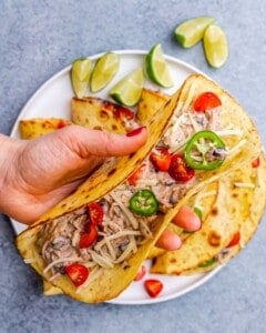 A fully assembled chicken taco filled with shredded chicken, beans, and toppings, placed on a plate with lime wedges.