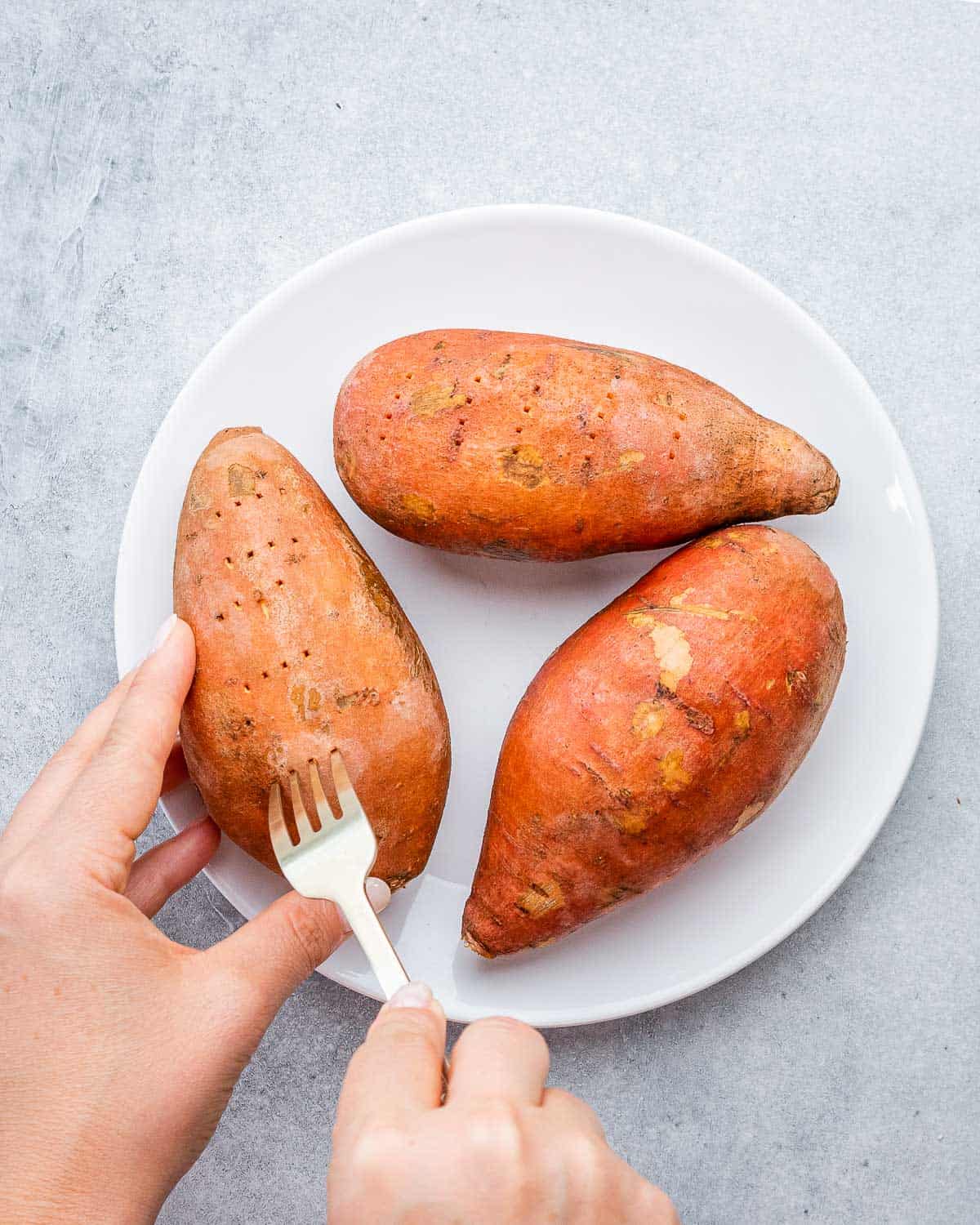 fork poking holes in sweet potatoes on a plate.