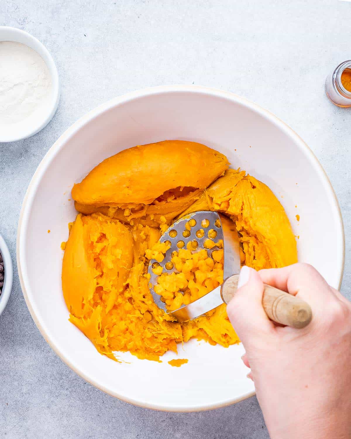 cooked sweet potatoes in a bowl being mashed with a masher.