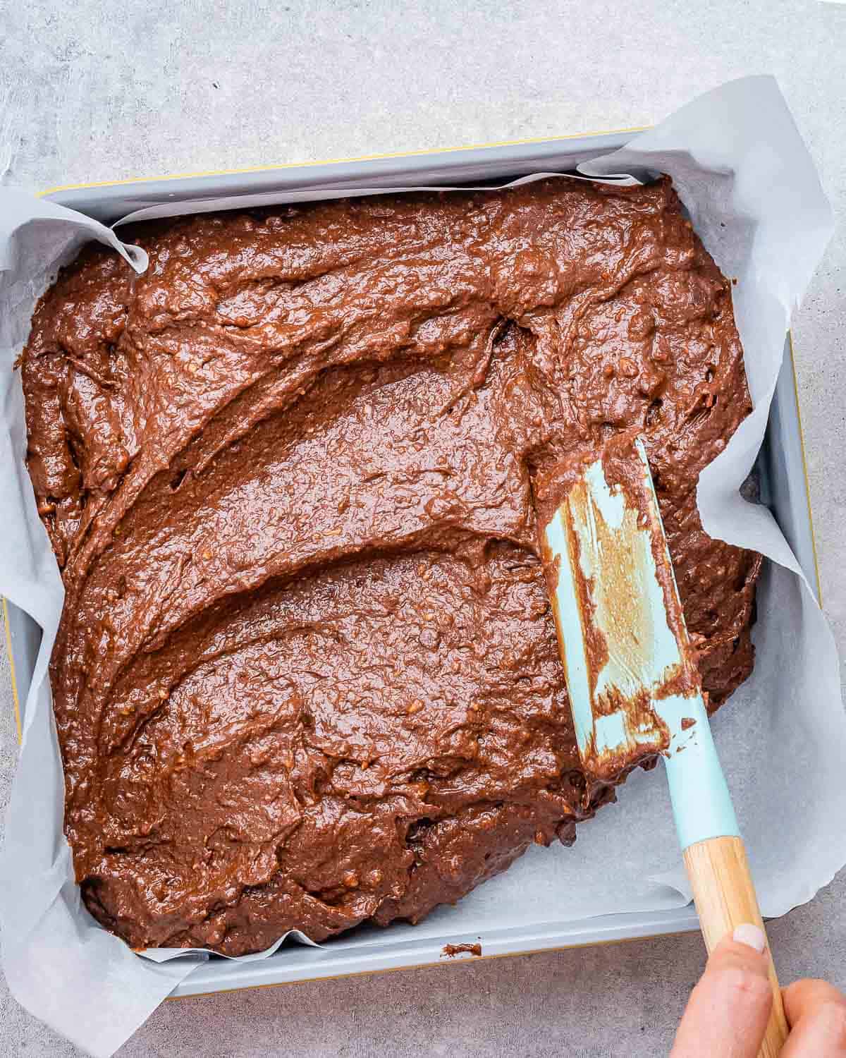 brownie batter is spread in a pan lined up with parchment paper.