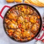 a red skilled filled with brown chicken stew and sauteed veggies.