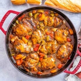 a red skilled filled with brown chicken stew and sauteed veggies.