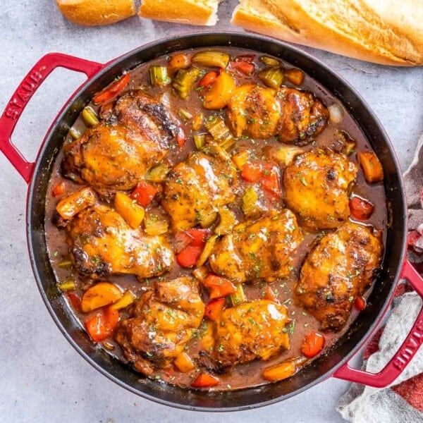 a red skilled filled with brown chicken stew and sauteed veggies.