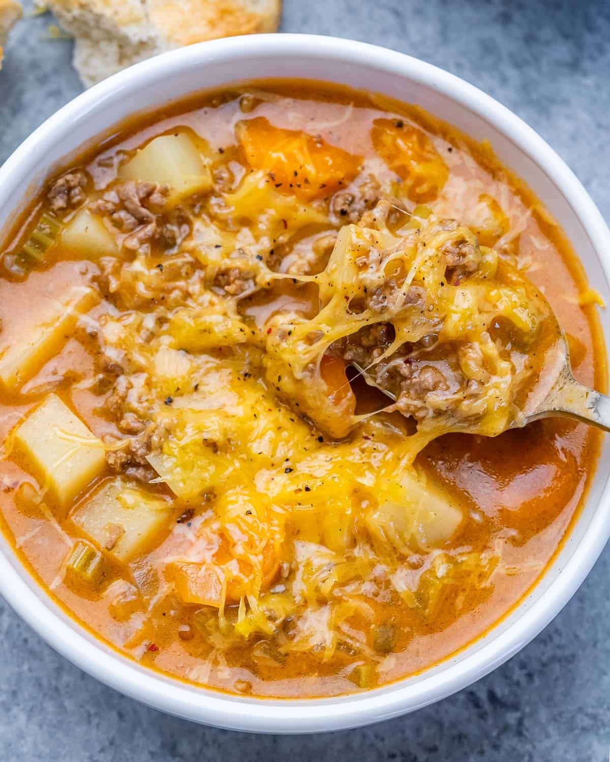 A white bowl of cheeseburger soup topped with cheese.