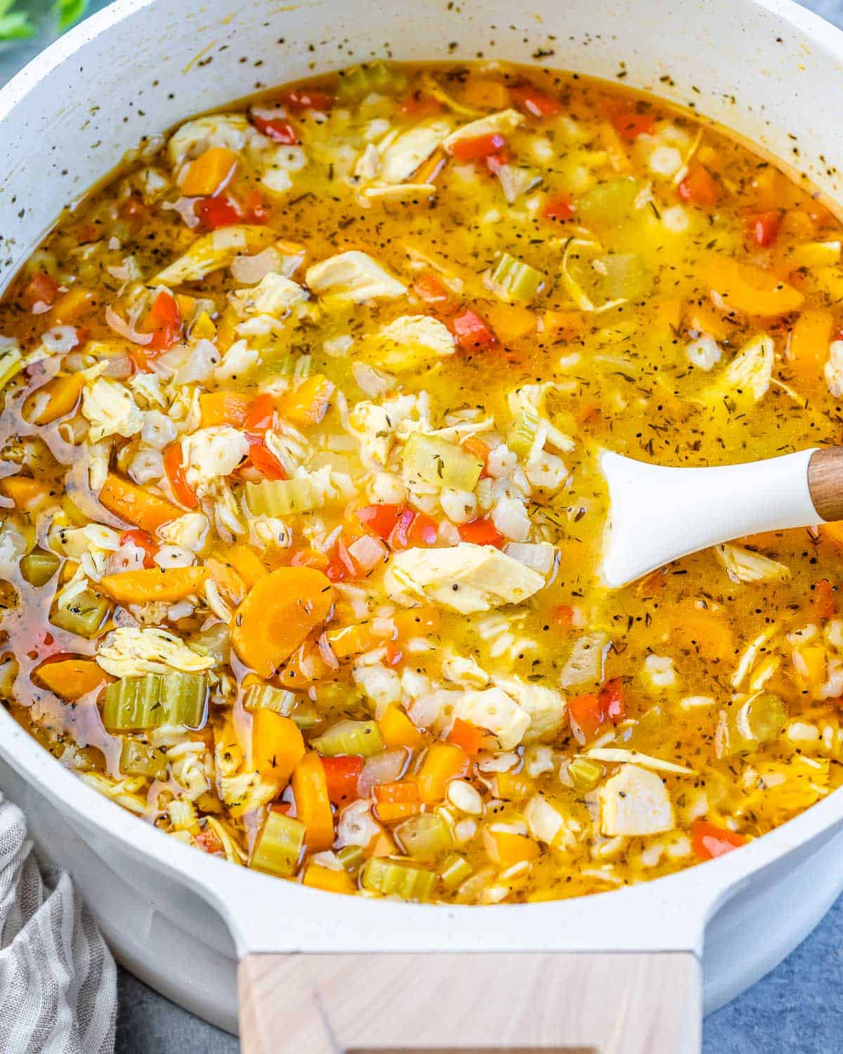 A white pot of chicken pastina soup with a serving spoon.