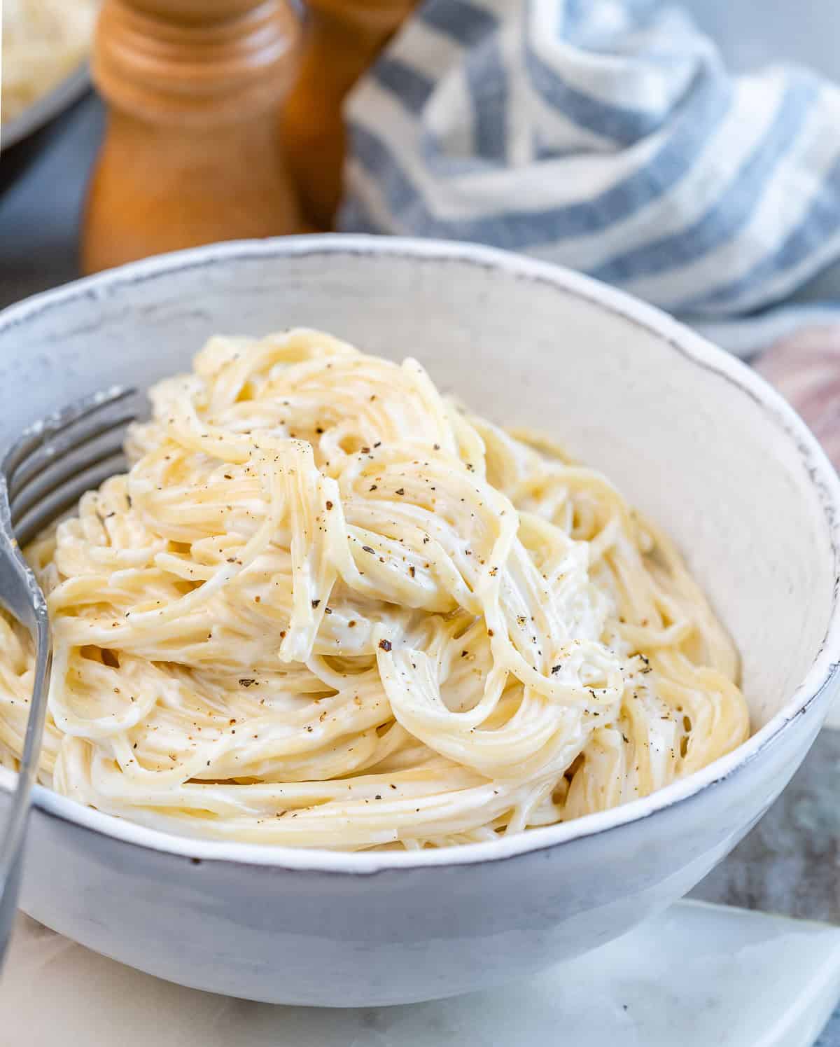 Side angle of a bowl of Alfredo pasta, with sauce visibly coating the noodles evenly.