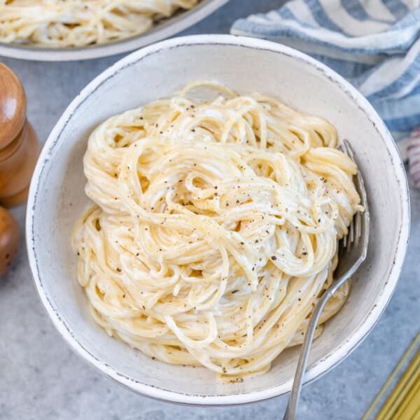 White bowl filled with spaghetti mixed with Alfredo sauce, showing smooth and creamy texture.