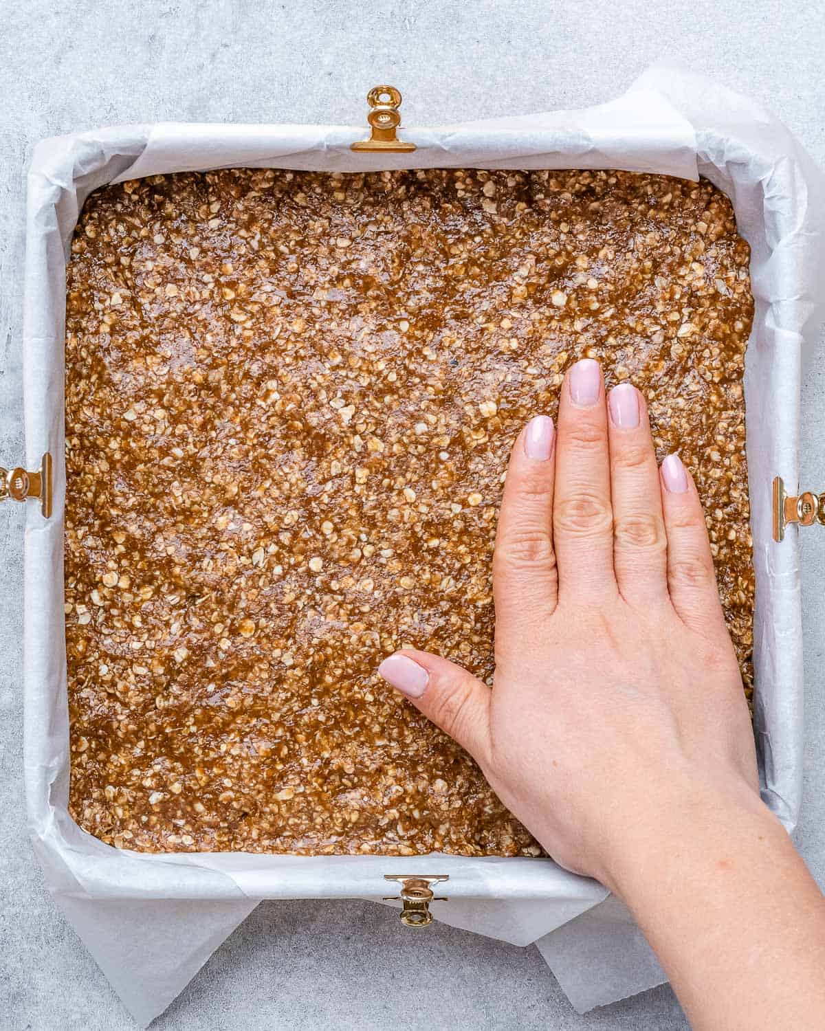 hand pressing down the oat base in a pan.