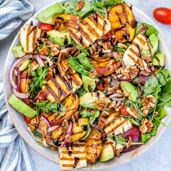 A round deep plate with salad topped with grilled halloumi and grilled peach and salad dressing drizzle.