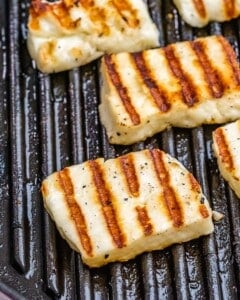 Halloumi slices grilling on a pan with golden brown grill marks.