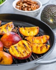 Close-up of grilled peach halves on a grill pan, developing dark charred grill marks.