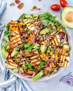 Summer salad with grilled peaches, sliced avocado, halloumi, red onion, cherry tomatoes, and pecans on mixed greens.