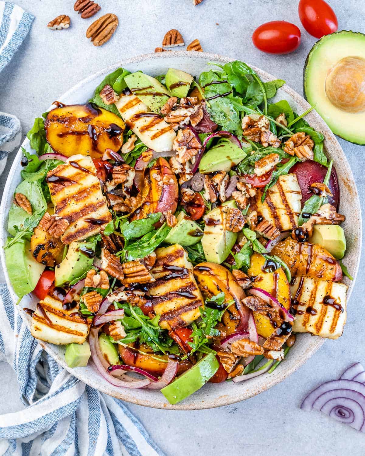 Summer salad with grilled peaches, sliced avocado, halloumi, red onion, cherry tomatoes, and pecans on mixed greens.