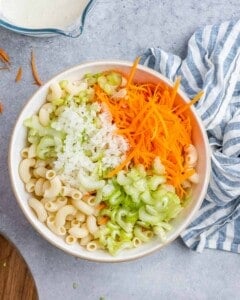 Elbow macaroni topped with grated carrot, chopped celery, and grated onion, ready for mixing.
