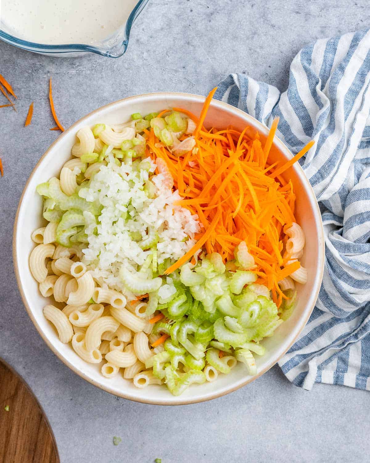 Elbow macaroni topped with grated carrot, chopped celery, and grated onion, ready for mixing.
