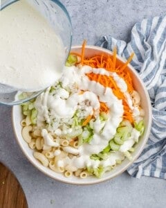 Pouring the mayo and milk dressing over the chopped veggies and macaroni in a mixing bowl.