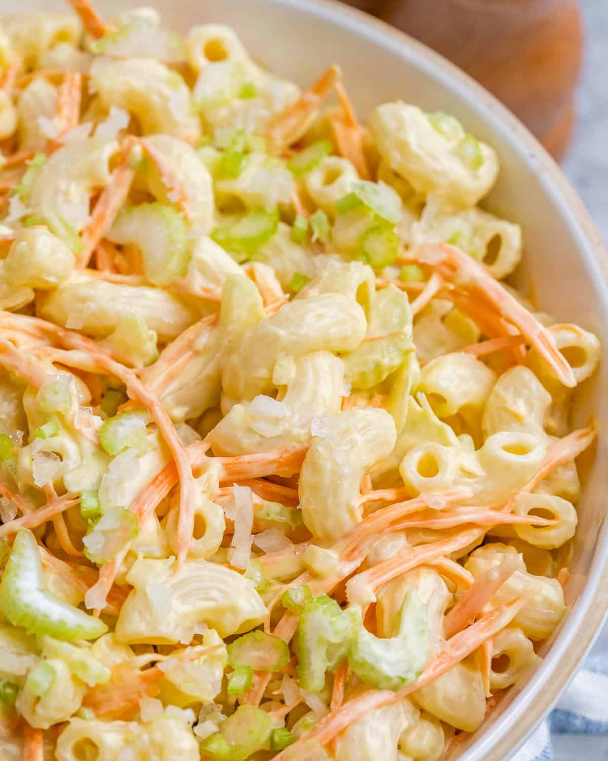 Zoomed-in view of macaroni salad with shredded carrots and chopped celery coated in creamy dressing.