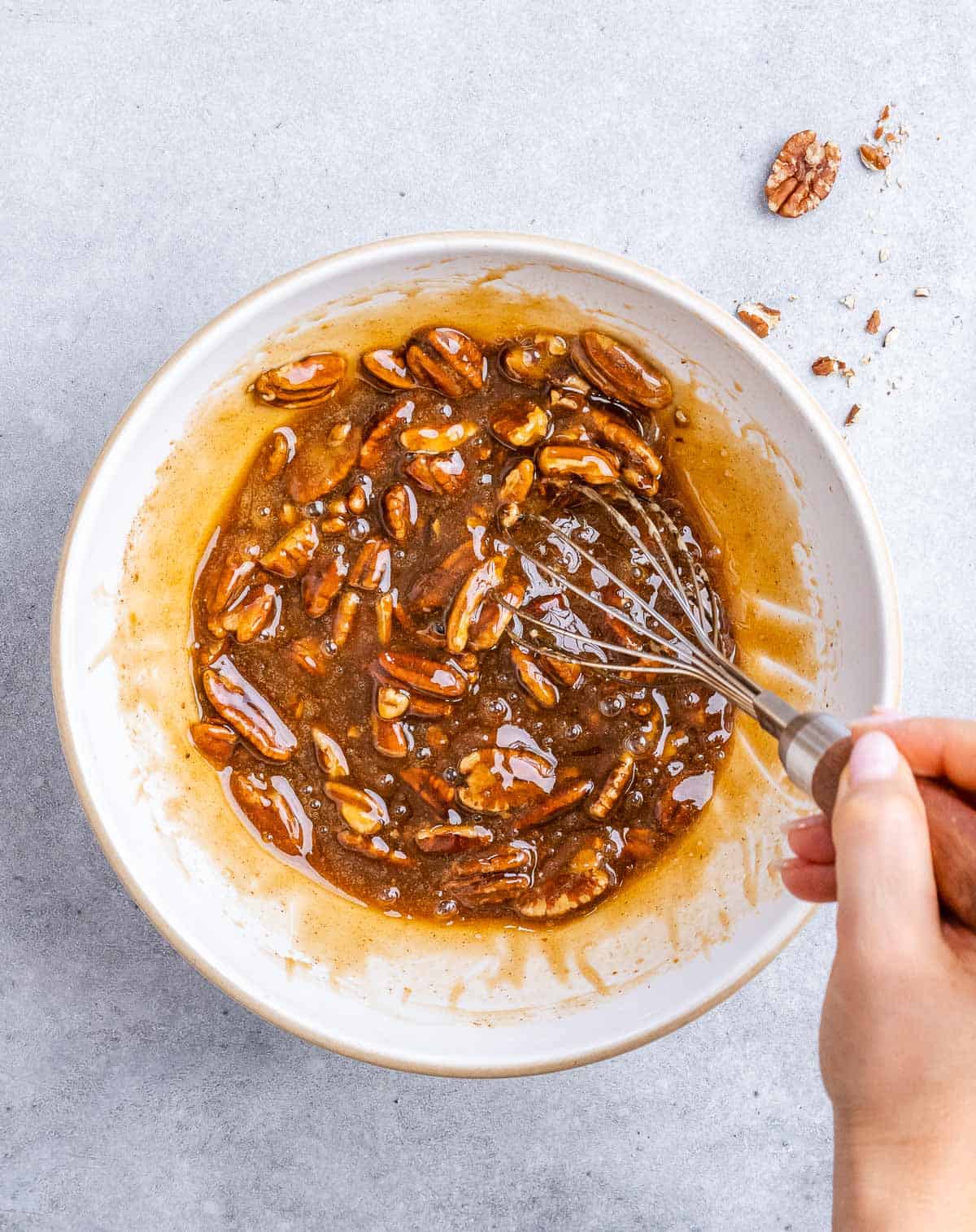 Stirring pecans with honey, egg, sugar mixture in a white bowl.