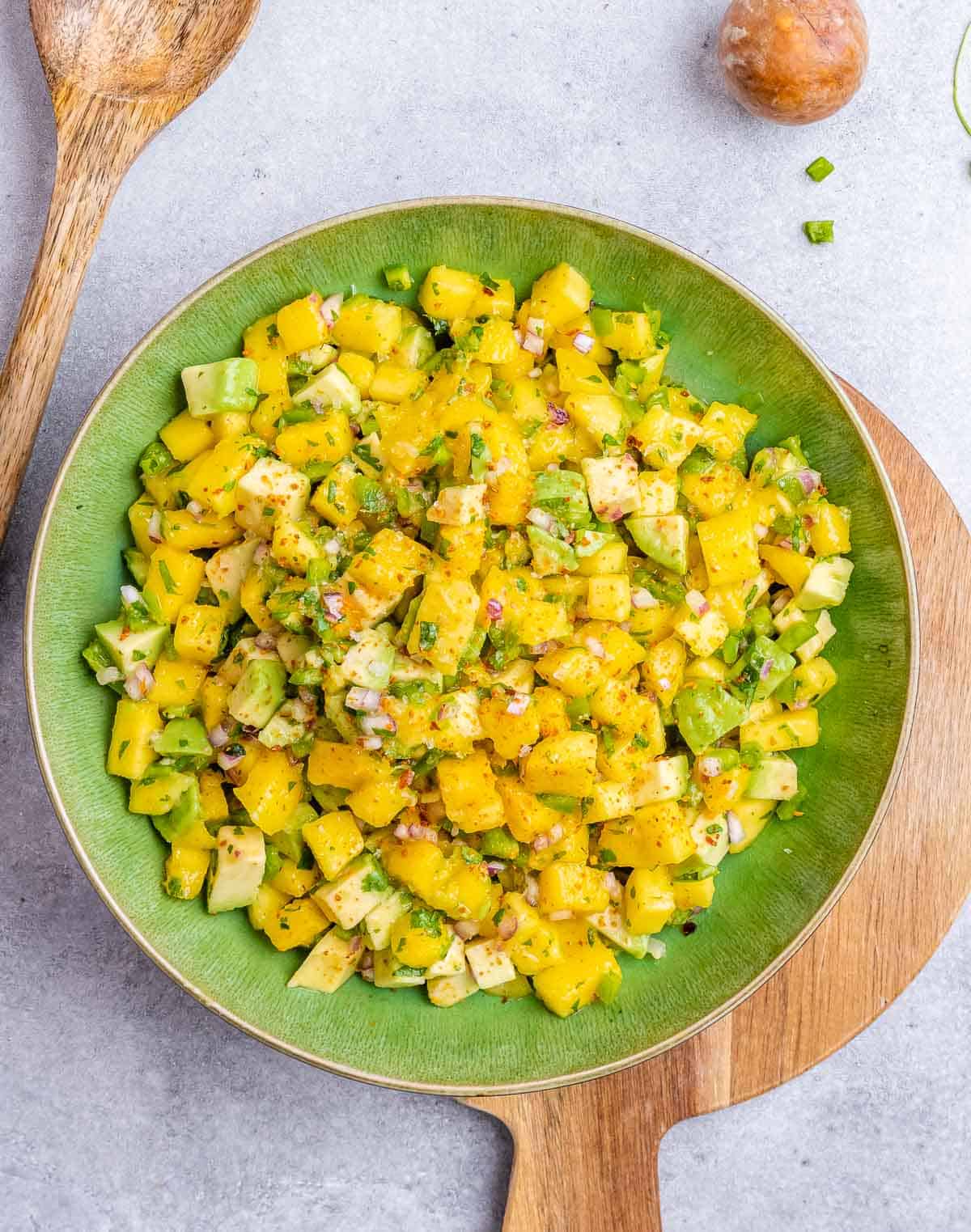 Mixed mango and veggies for salsa on a green bowl.