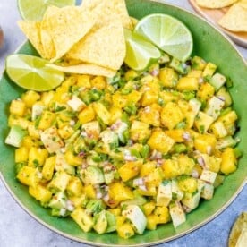 a greed round bowl with mango salad and a few tortilla chips.
