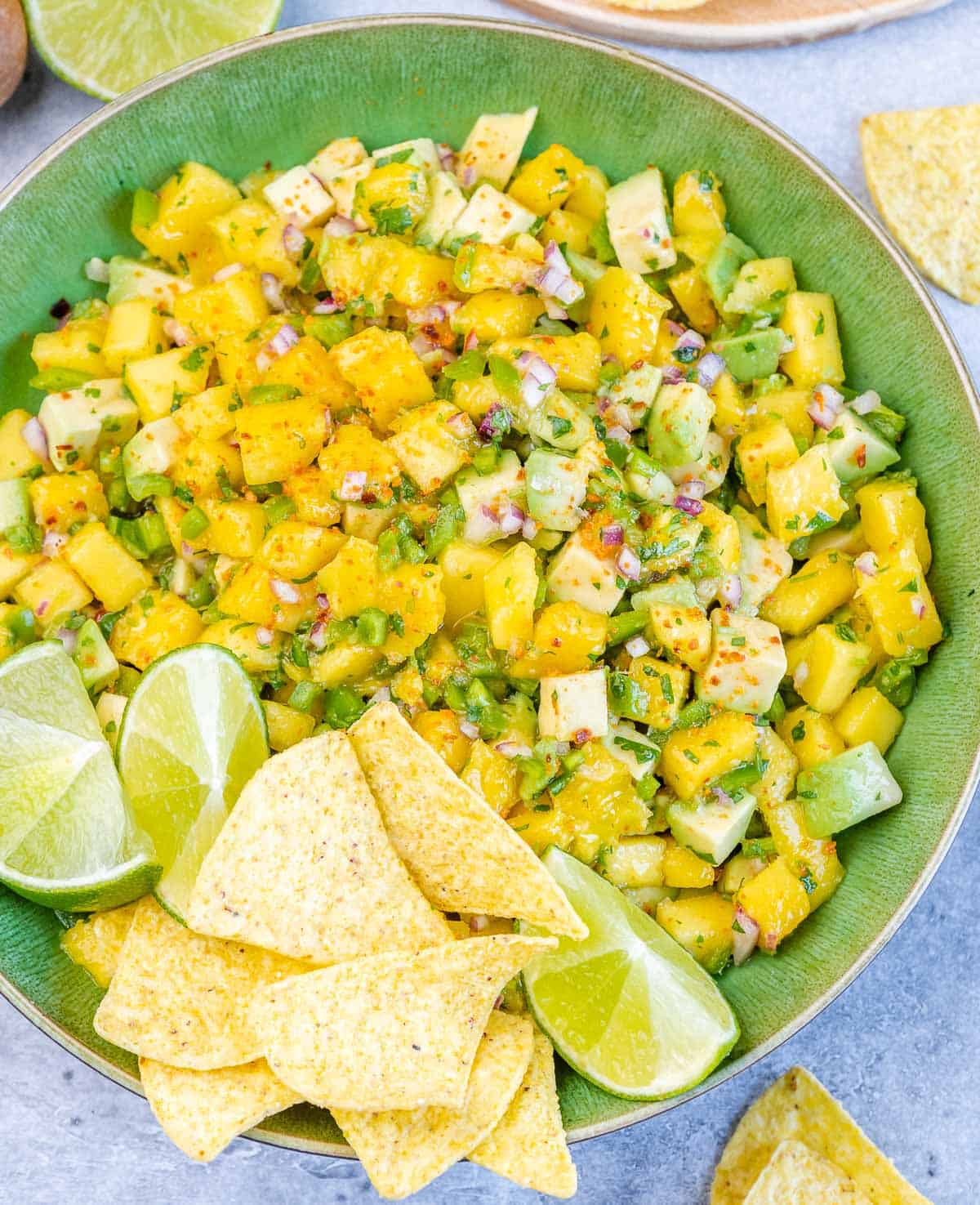Mango salsa on a green bowl with chips and lime wedges.