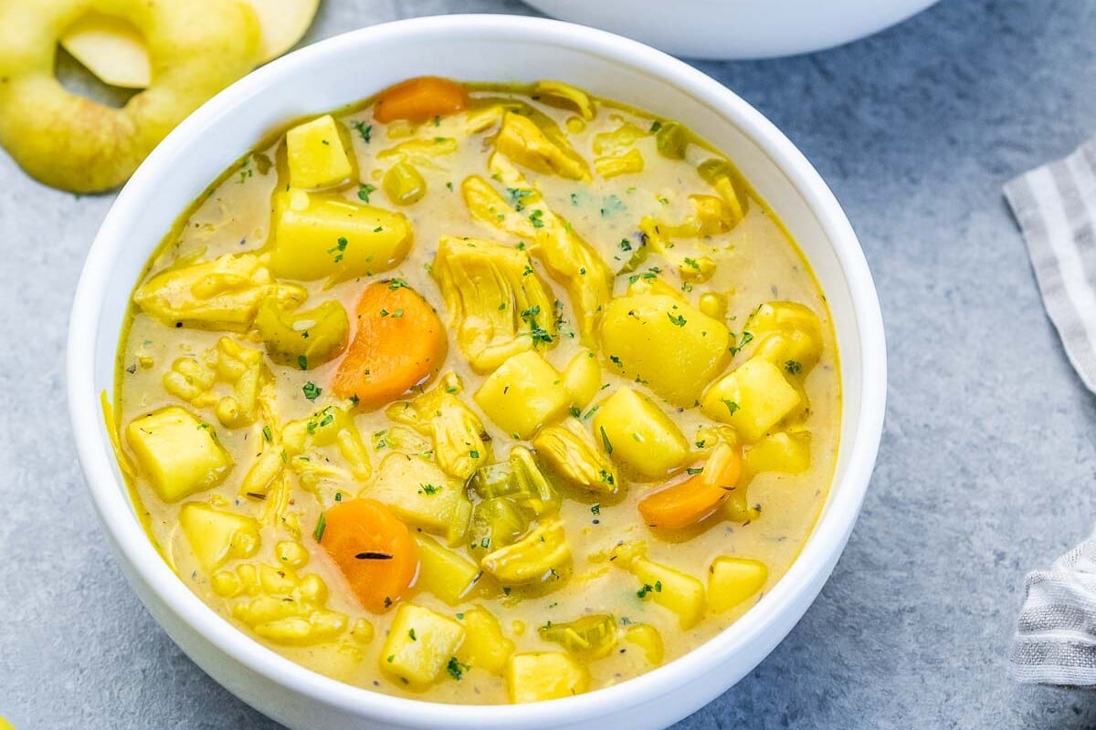 A white bowl of mulligatawny soup with a spoon