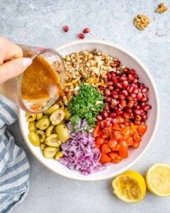 Dressing being poured over the salad ingredients in the bowl.