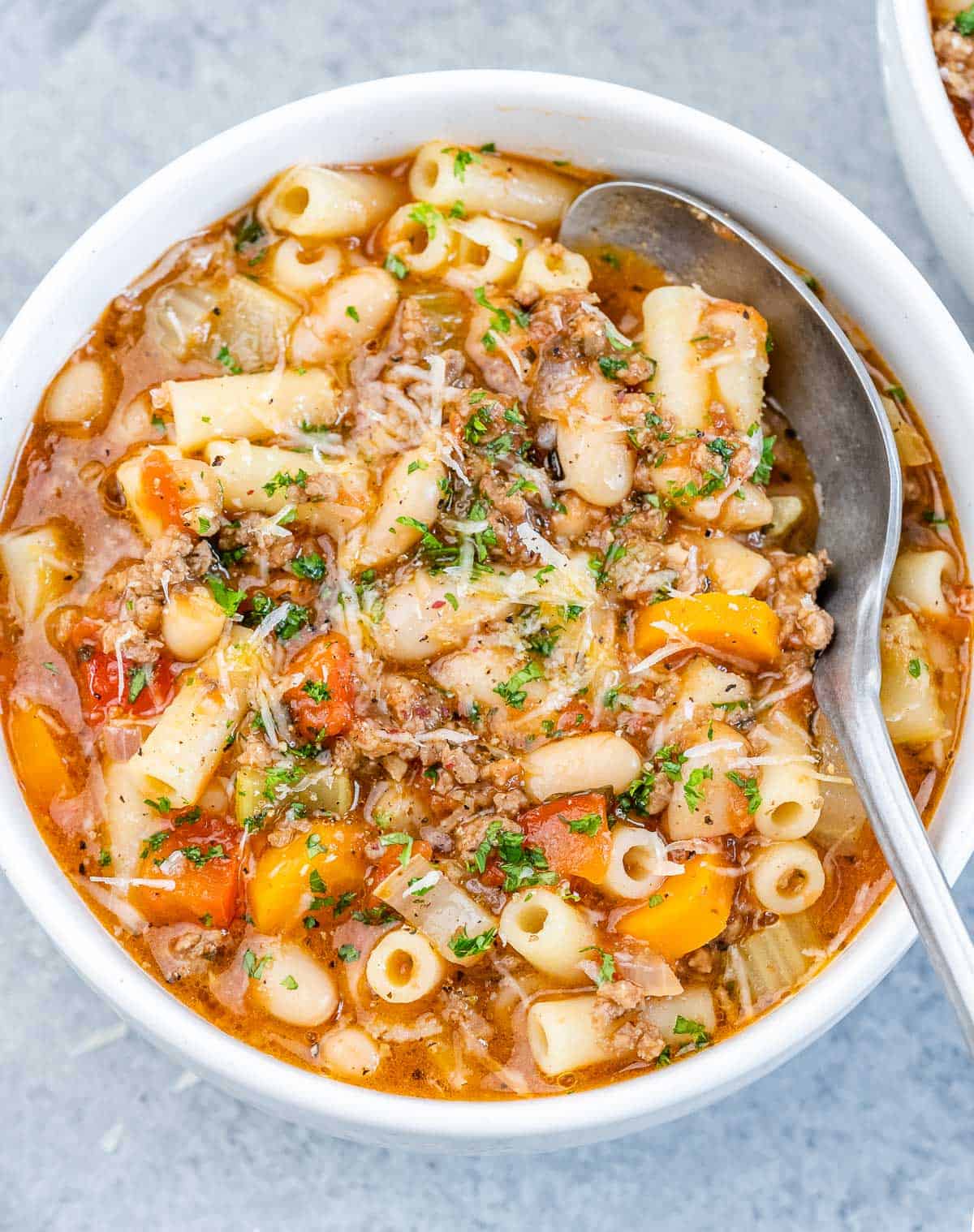 A white bowl of pasta fagioli soup with a spoon.