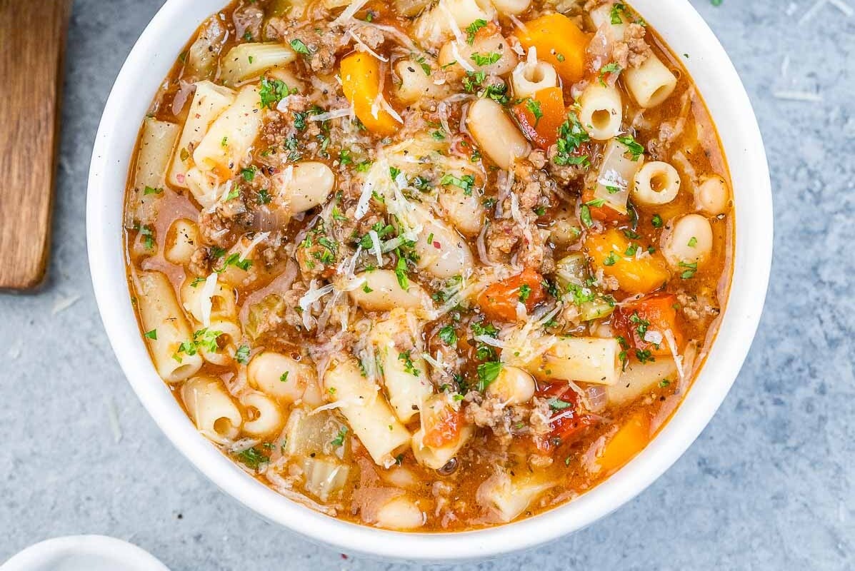 Three white bowls of pasta fagioli soup on a grey background.