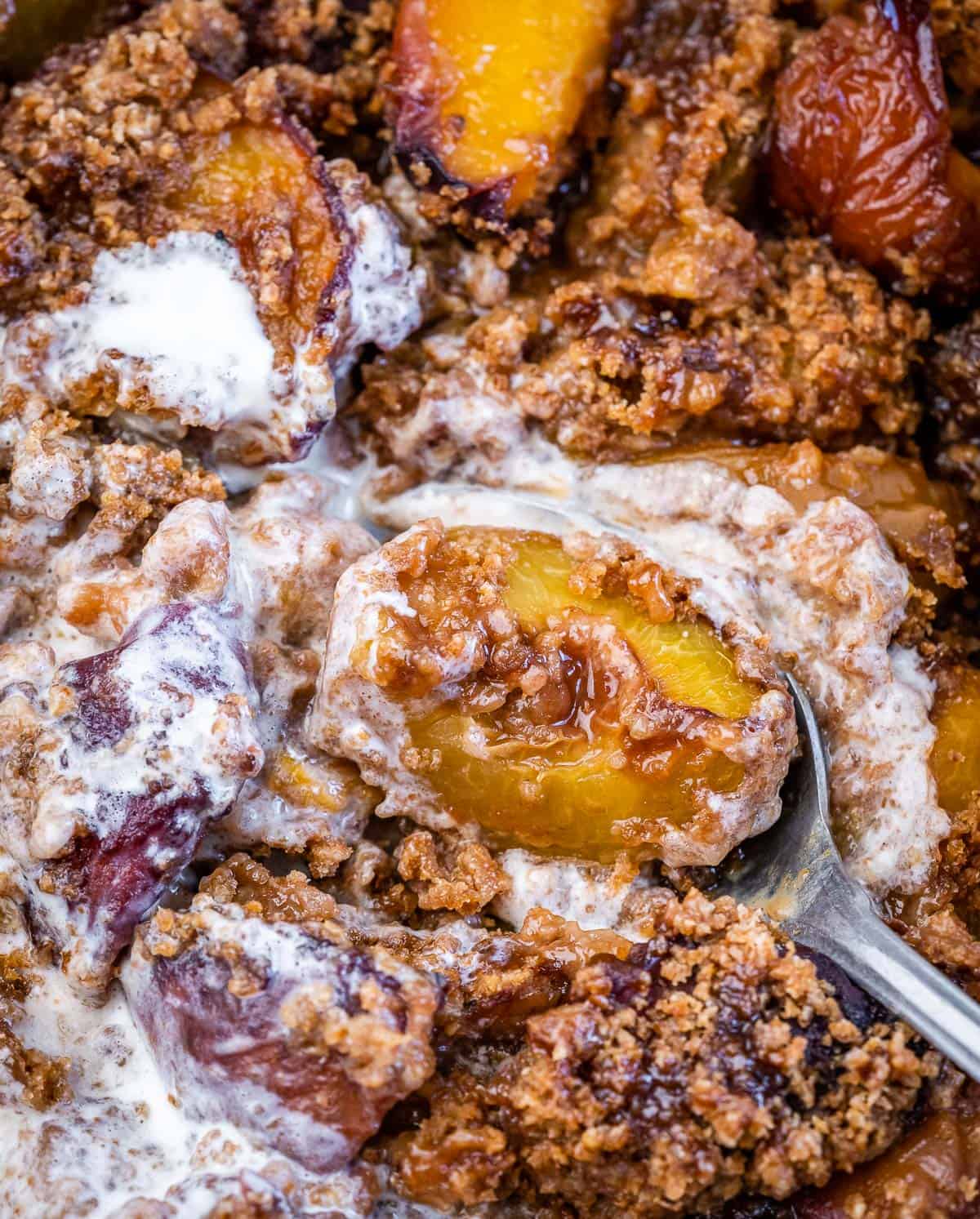 Serving spoon dishing into a peach cobbler with melted vanilla ice cream.