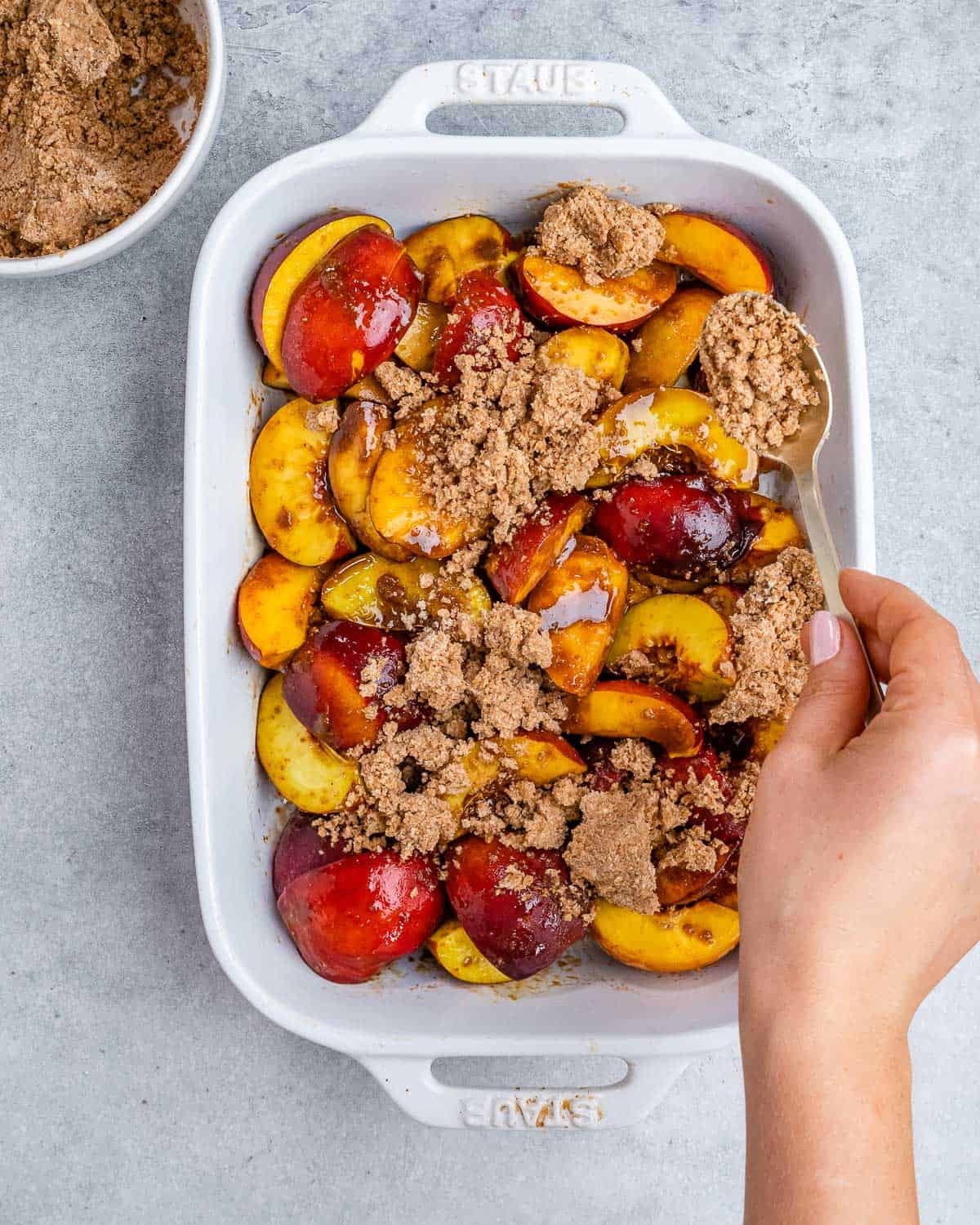 Adding the cobbler topping over sliced peaches.