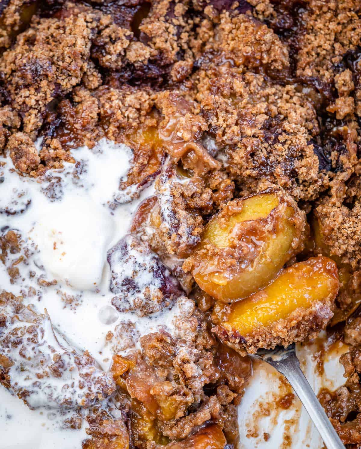 a spoon grabbing a serving of peach cobbler from the dish.