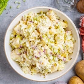 Finished potato salad in a white bowl, garnished with cracked black pepper, ready for serving.