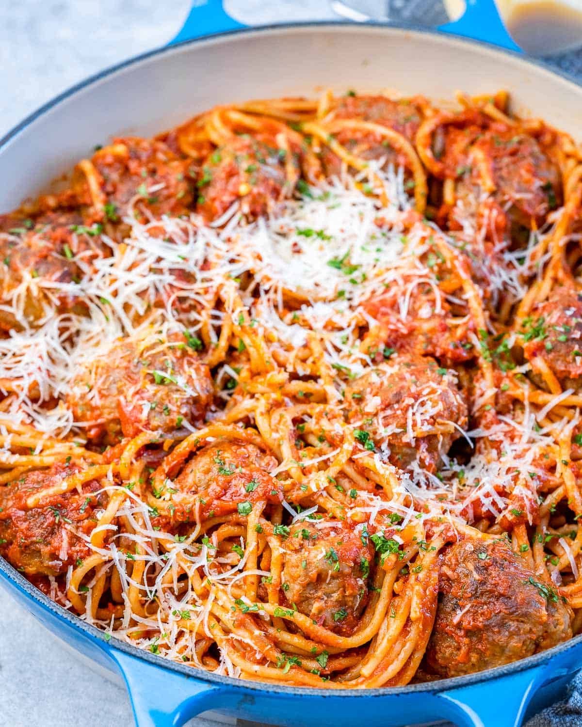 Top-down view of spaghetti meatballs in a large pot with melted parmesan and herbs.