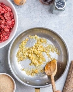 Finely diced onions and minced garlic sautéing in a skillet with olive oil, stirred with a wooden spoon until soft and golden.