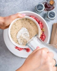 Pouring milk into a bowl of breadcrumbs and seasonings to create the meatball binder.
