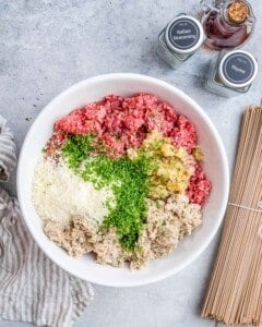 Ingredients for the meatballs in a bowl: ground beef, parsley, breadcrumbs, and grated cheese.