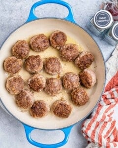 Meatballs browning in a skillet over medium heat, developing a golden crust.