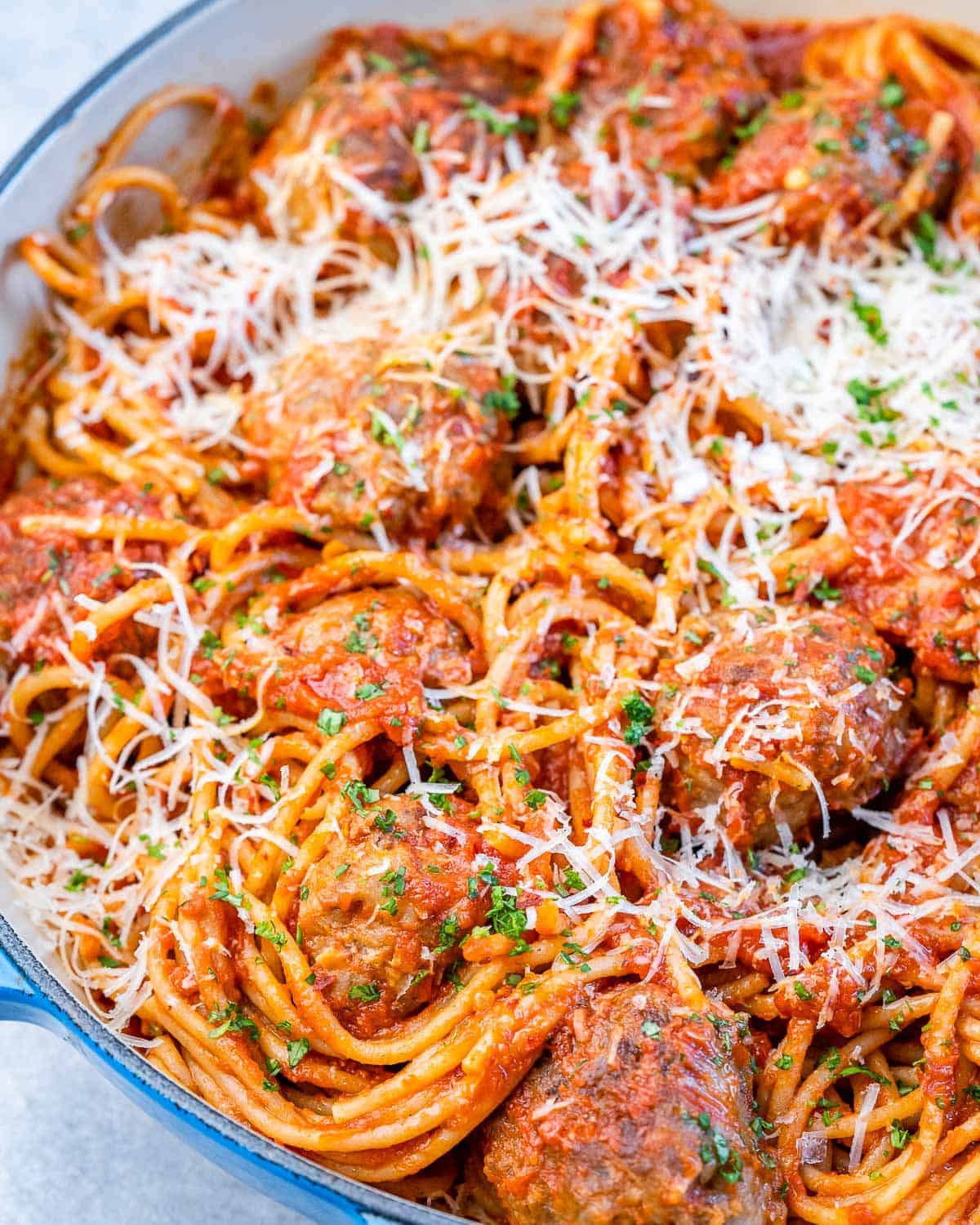 Closer view of spaghetti meatballs in a large pot with melted parmesan and herbs.