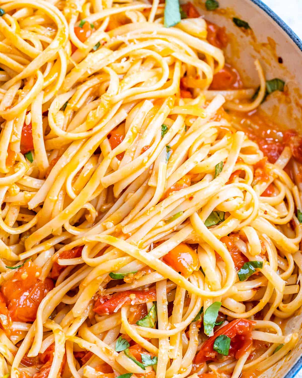 Pasta being tossed into the skillet with tomato basil sauce using kitchen tongs.