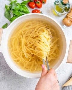 Cooked spaghetti lifted from pot with tongs.