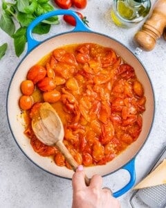 Cherry tomatoes bursting in olive oil in skillet.