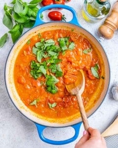 Tomato basil sauce cooking in skillet with fresh basil.
