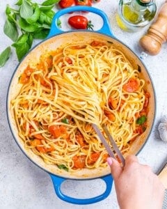 Spaghetti and tomato basil sauce fully combined in the skillet, with flecks of fresh basil.