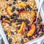 A white baking dish filled with baked blueberry and peach topped with an oatmeal crisp mix.