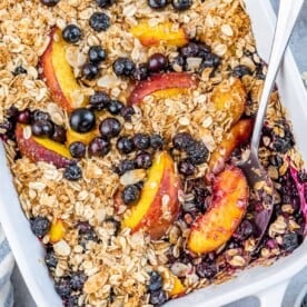 A white baking dish filled with baked blueberry and peach topped with an oatmeal crisp mix.