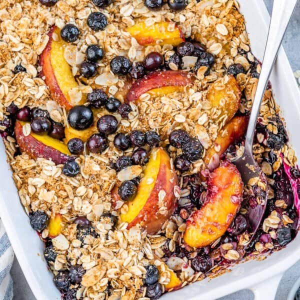 A white baking dish filled with baked blueberry and peach topped with an oatmeal crisp mix.