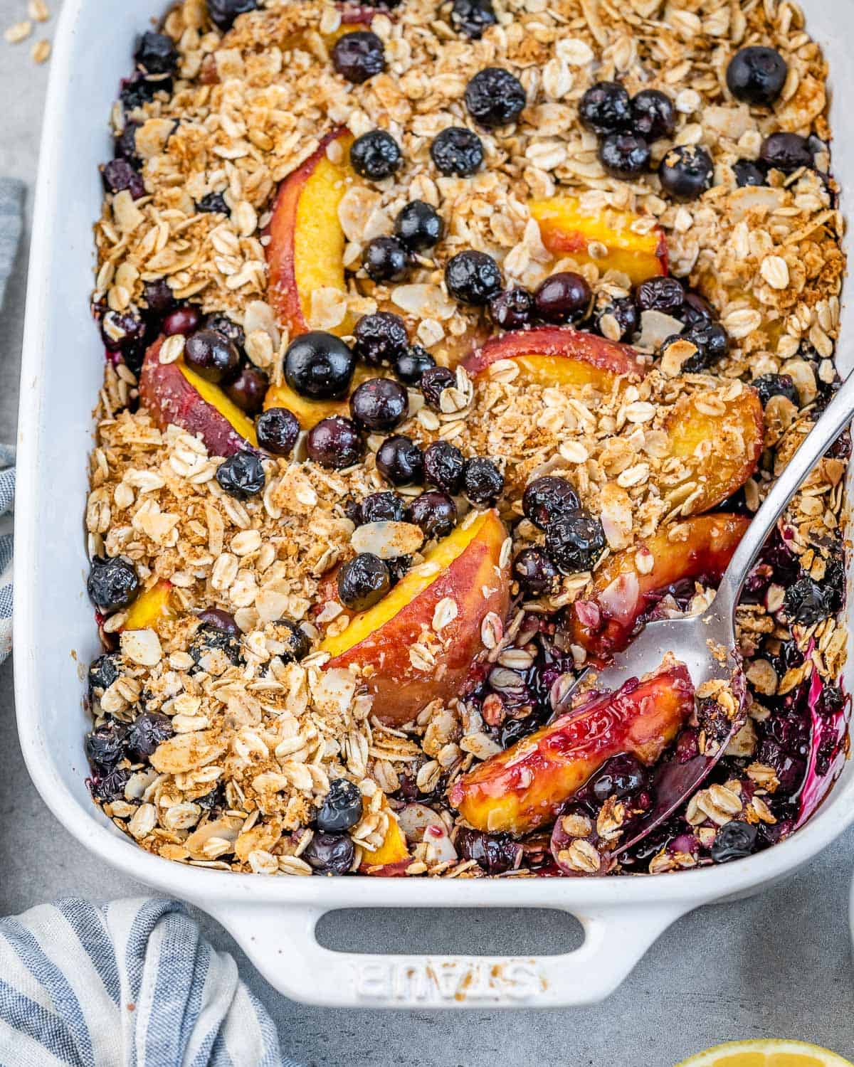 A white baking dish filled with baked blueberry and peach topped with an oatmeal crisp mix.